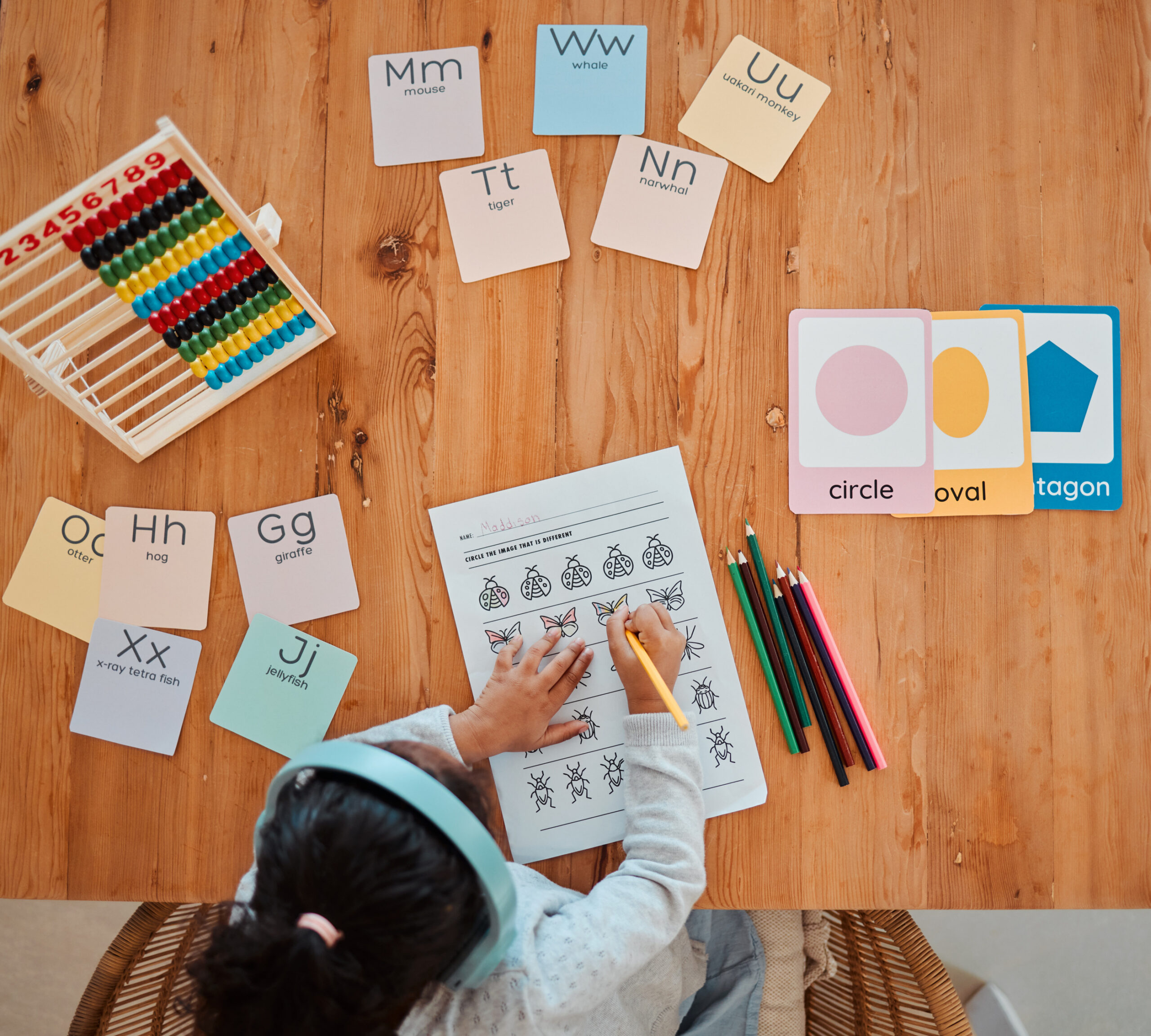 Child working on a math worksheet with colorful pencils, letter and shape cards, and an abacus on a wooden table. Text overlay: "9 Ways to Grow Your Homeschoolers Love of Math."