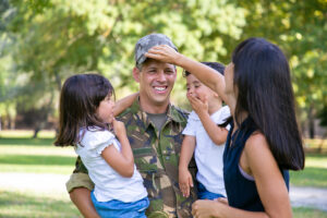 A man in military camo lifts a smiling child outdoors, surrounded by trees. Text below reads “What the Federal COMPASS Act Could Mean for Homeschooling Nationwide.”