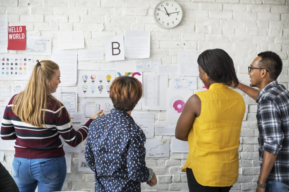 Four people analyze charts and diagrams on a wall, conveying teamwork and focus.