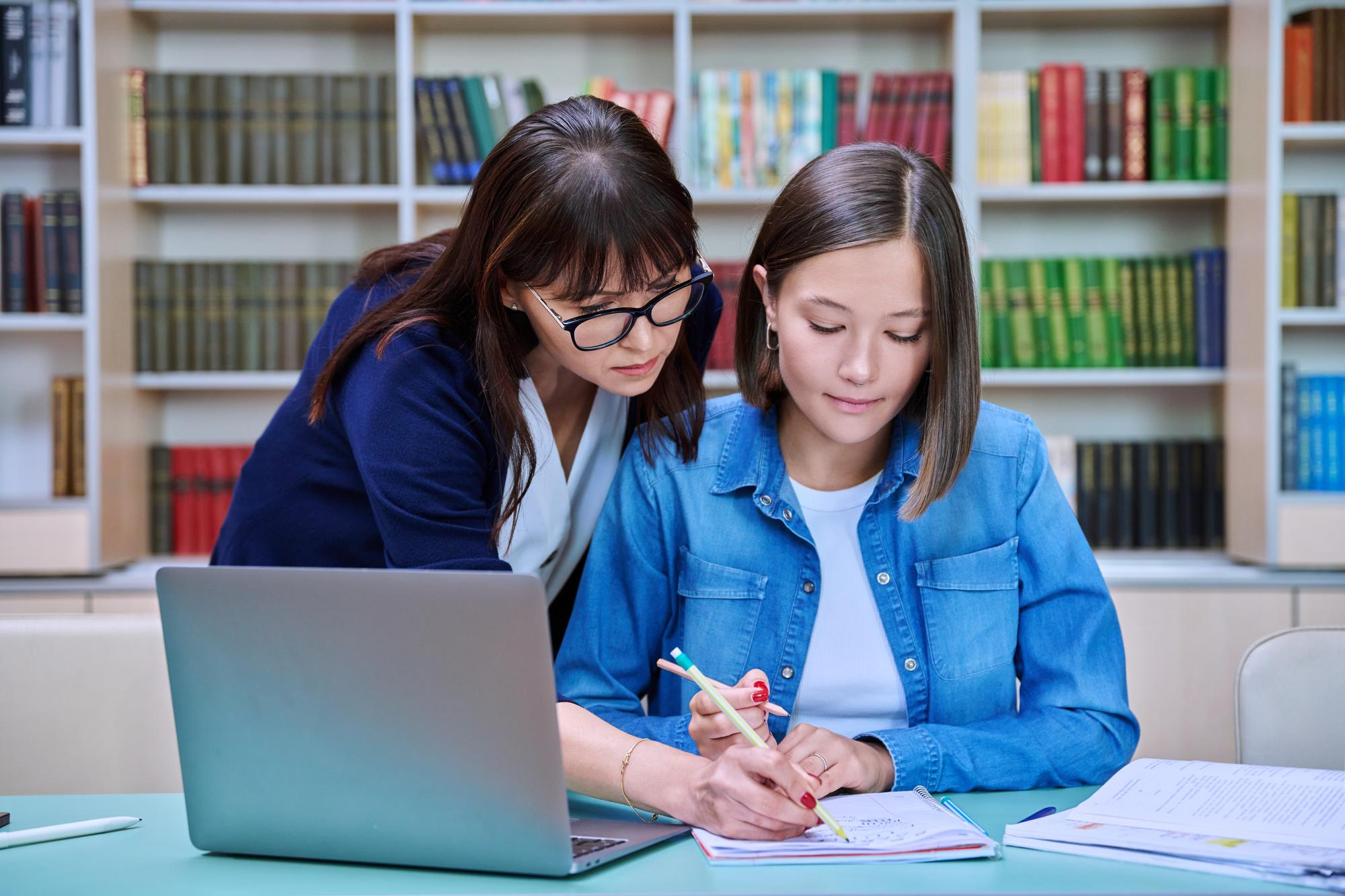 A tutor and student sit at a table working on homework.