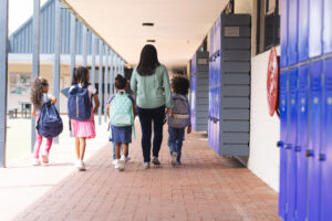 A woman walks with four children carrying backpacks down a school hallway; text reads, "New Hampshire’s New Law Could Be A Turning Point For Homeschoolers.