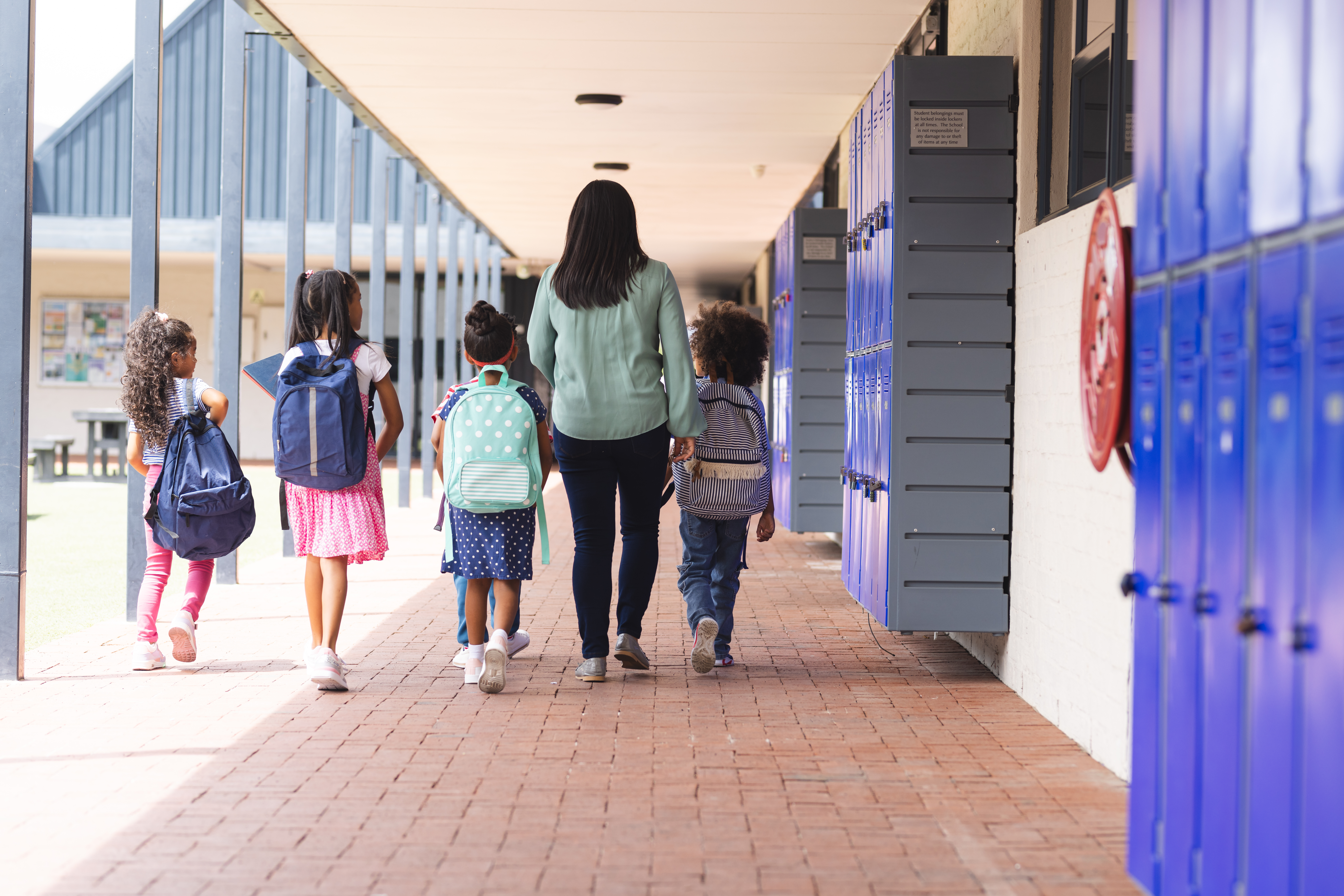 A woman walks with four children carrying backpacks down a school hallway; text reads, "New Hampshire’s New Law Could Be A Turning Point For Homeschoolers.
