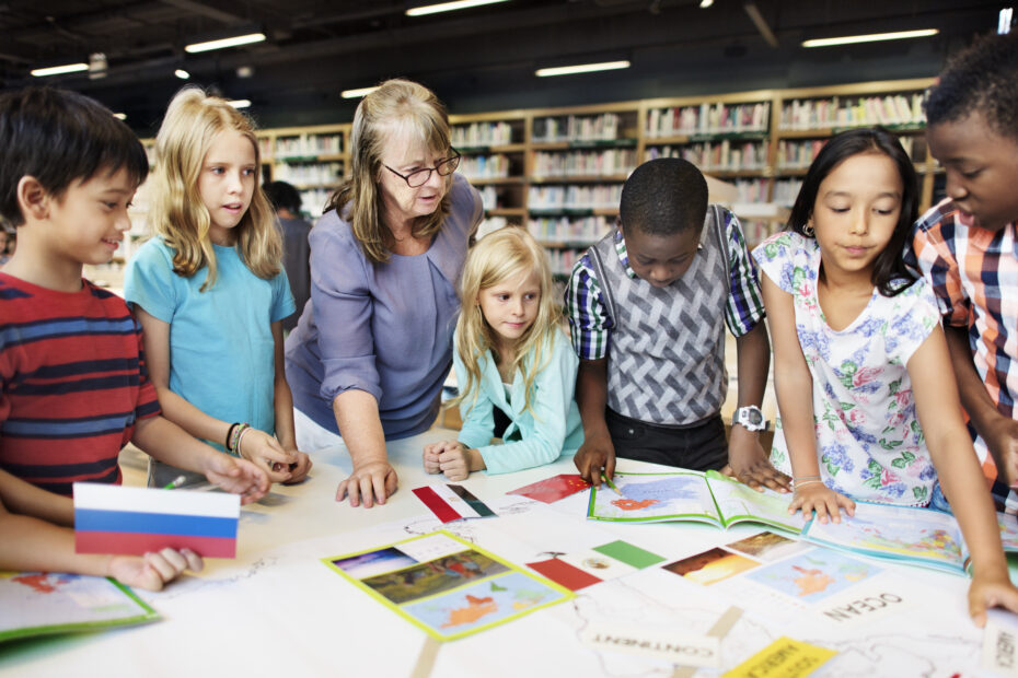 Class of students and teacher gather around a table reviewing state flags, indicating the use of ESA funds. Title at bottom reads:Arkansas’ Educational Freedom Accounts (EFA) Undergoes Major Updates
